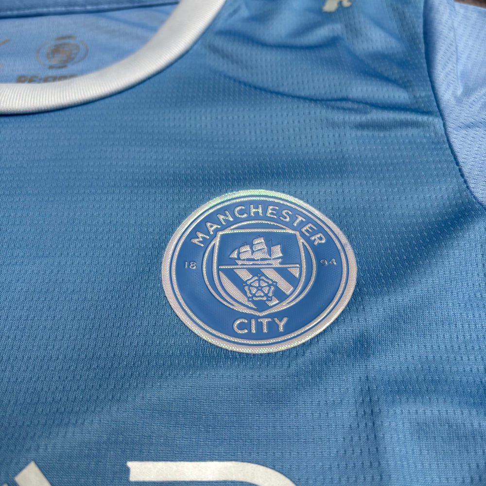 Kit Infantil Manchester City I 2026/27 Azul-Celeste Camisa e Shorts - detalhe do escudo bordado